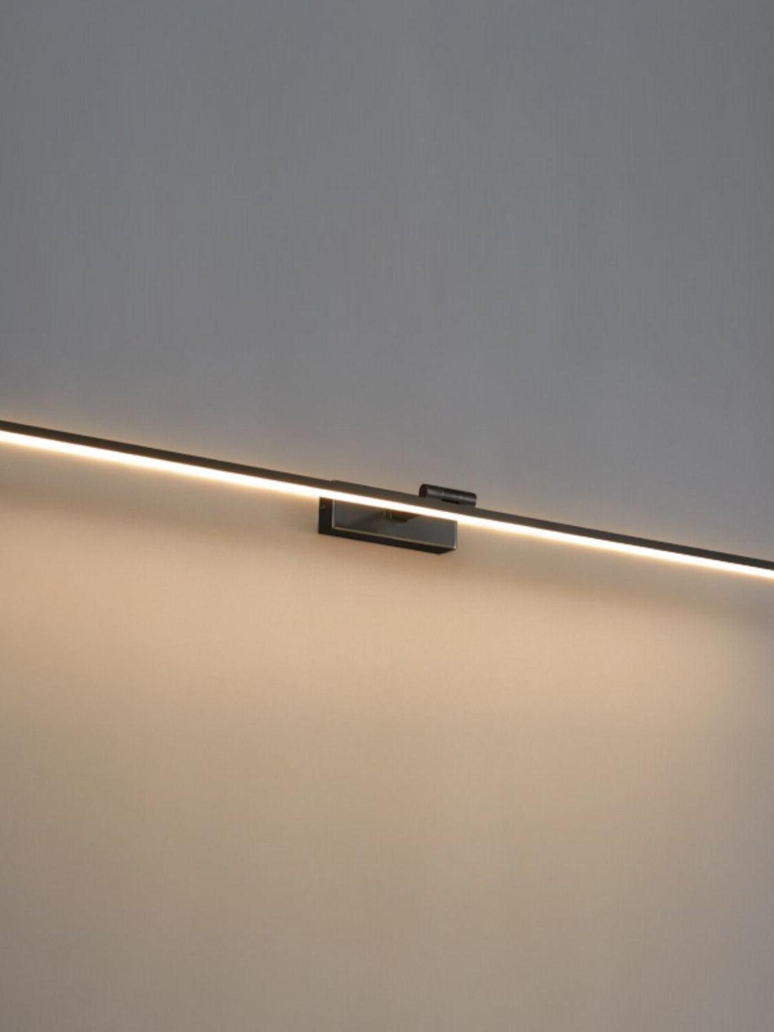 Illuminated black linear wall light with rectangular wallplate and pale underside strip against grey wall