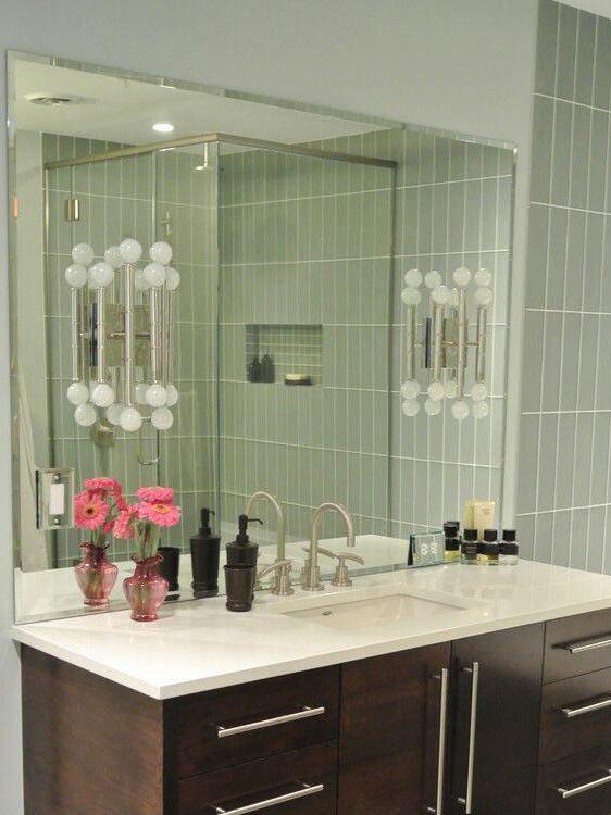 Chrome Meurice wall light beside a bathroom vanity mirror on green tiles above a white basin and dark cabinet