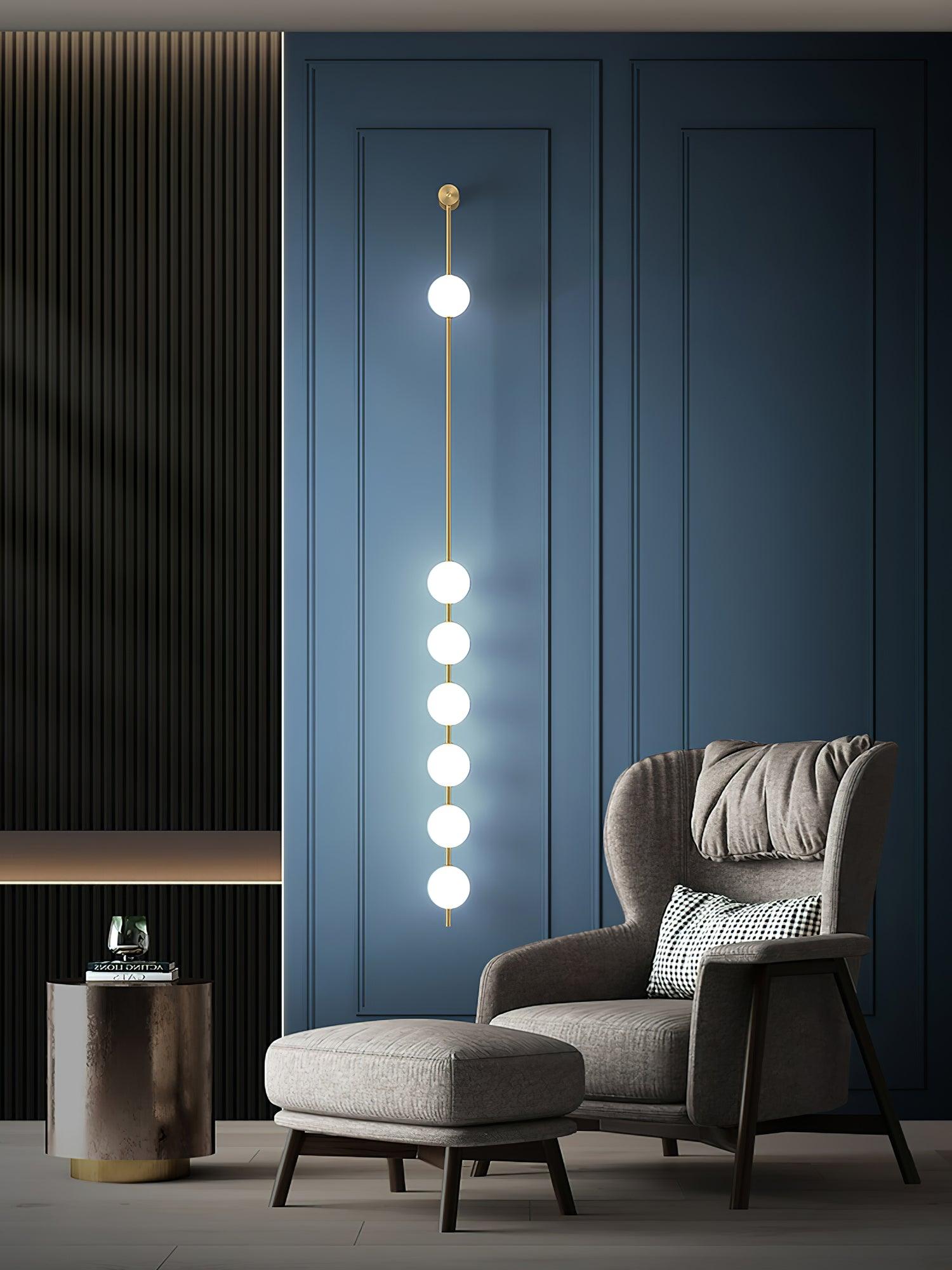 Seven-globe wall light on a blue panelled wall beside an upholstered armchair, footstool and side table