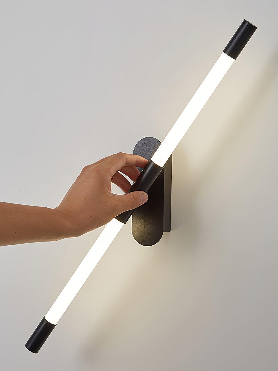 A hand holding the centre of an angled black Agnes wall light beside its wall plate