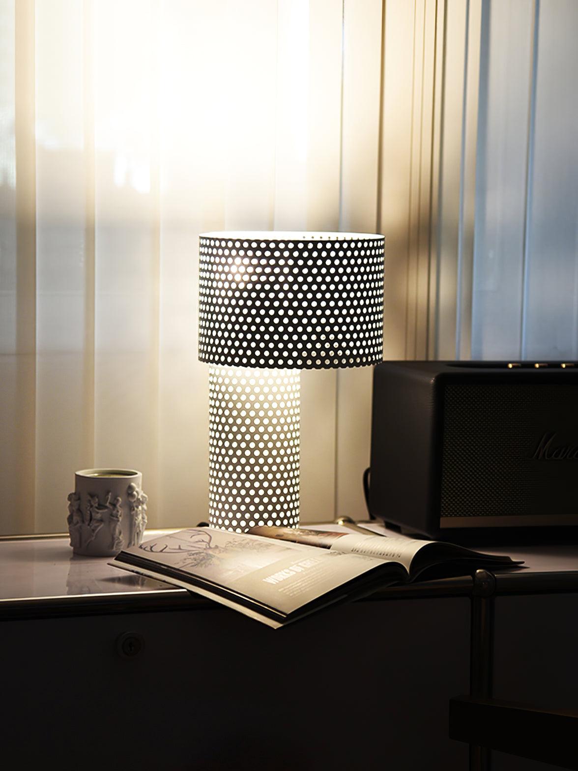 Lit perforated lamp by mug and papers on desk