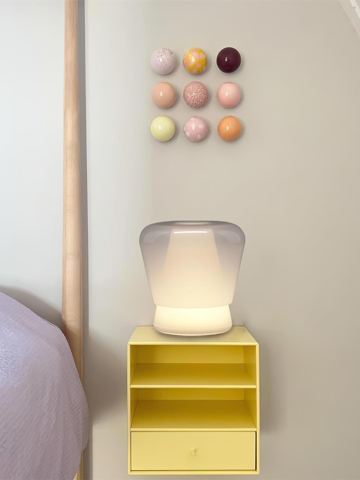 White Jumelle lamp lit on yellow bedside cabinet