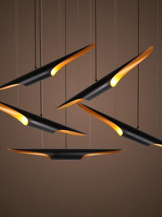 Black and gold horizontal ceiling pendants suspended on thin cords against a dark ceiling and brown wall