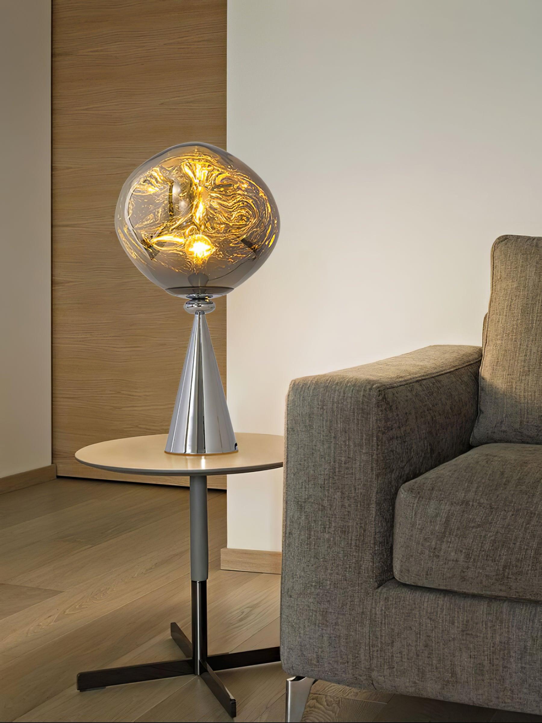 Glowing chrome globe table lamp on a round side table beside a gray armchair and wood door