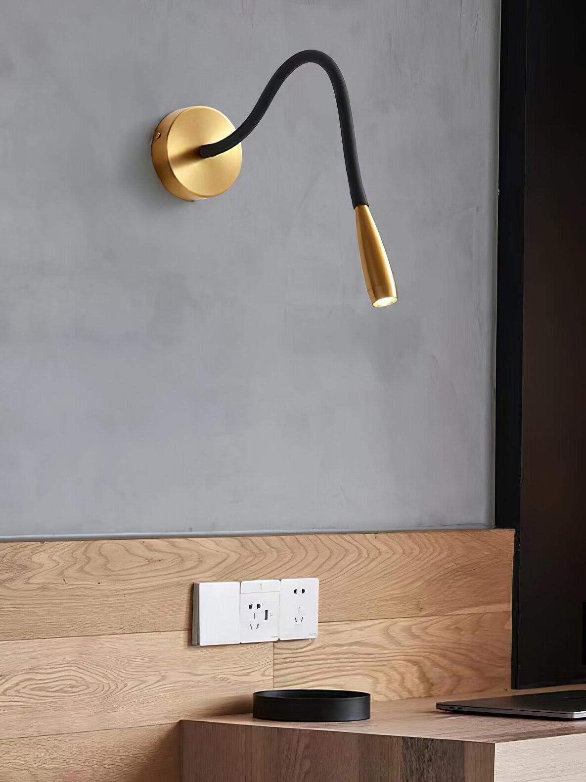 Gold Flexi above a wooden desk panel with wall sockets, a laptop and a black round object on the surface