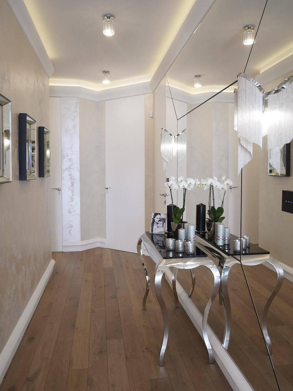 Chain-fringe chandelier in a bright hallway with mirrors and clear console chairs