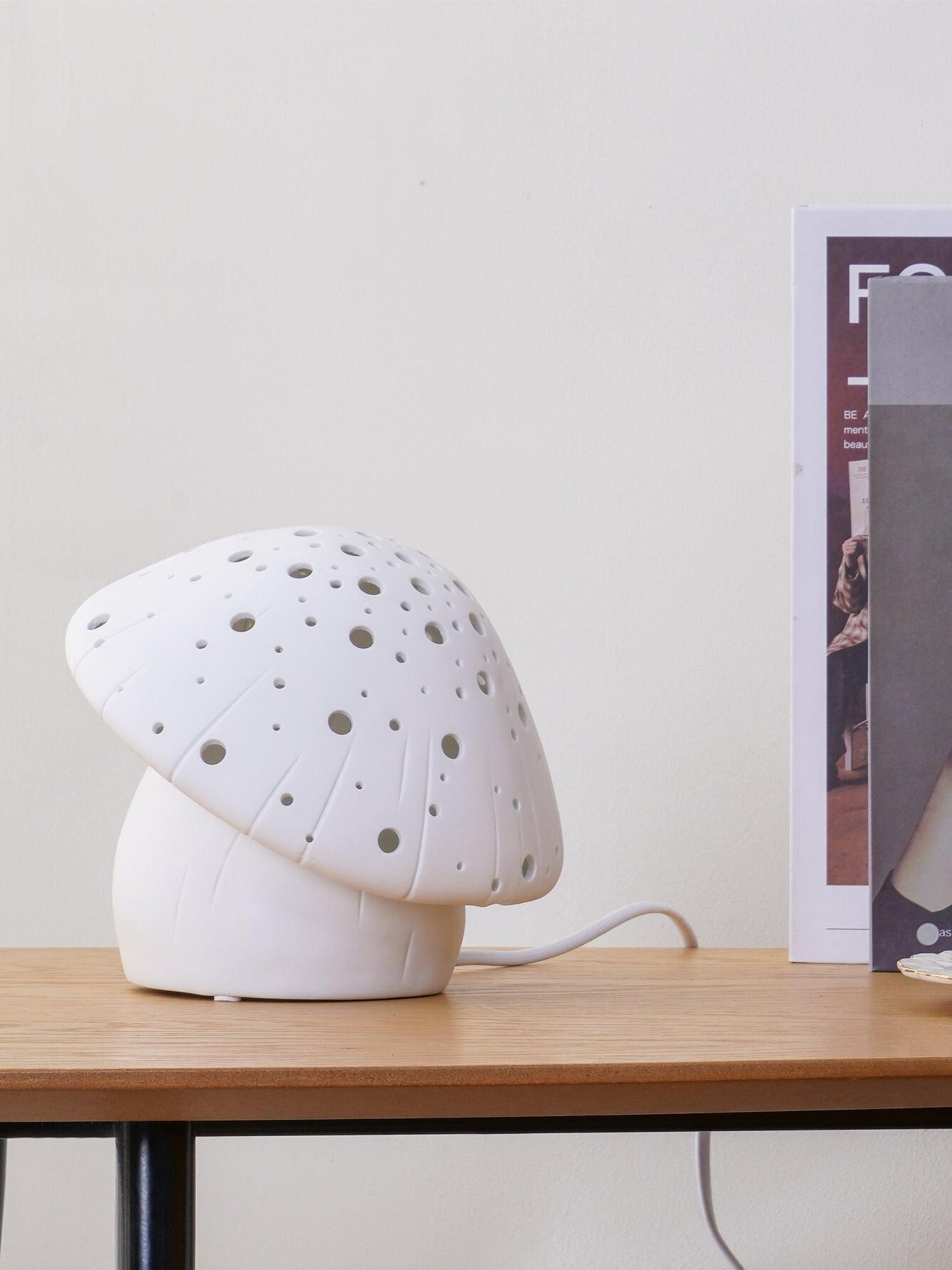 Unlit white Fungo lamp with a perforated mushroom cap and cable beside books on a table