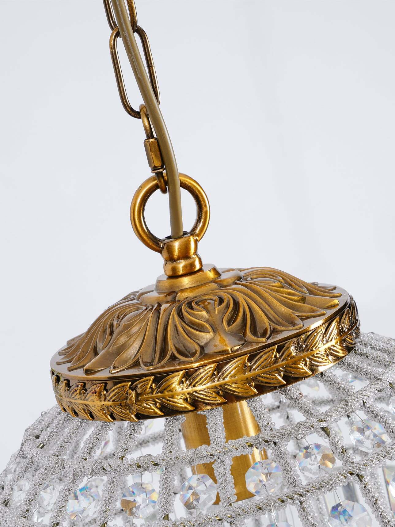 Close view of the chain link, ring, cable and carved leaf-pattern top cap with a reflective gold-tone edge