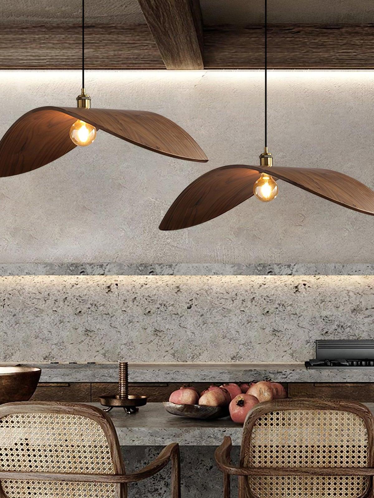 Two separate wood-tone curved pendants above a kitchen counter with woven-back chairs