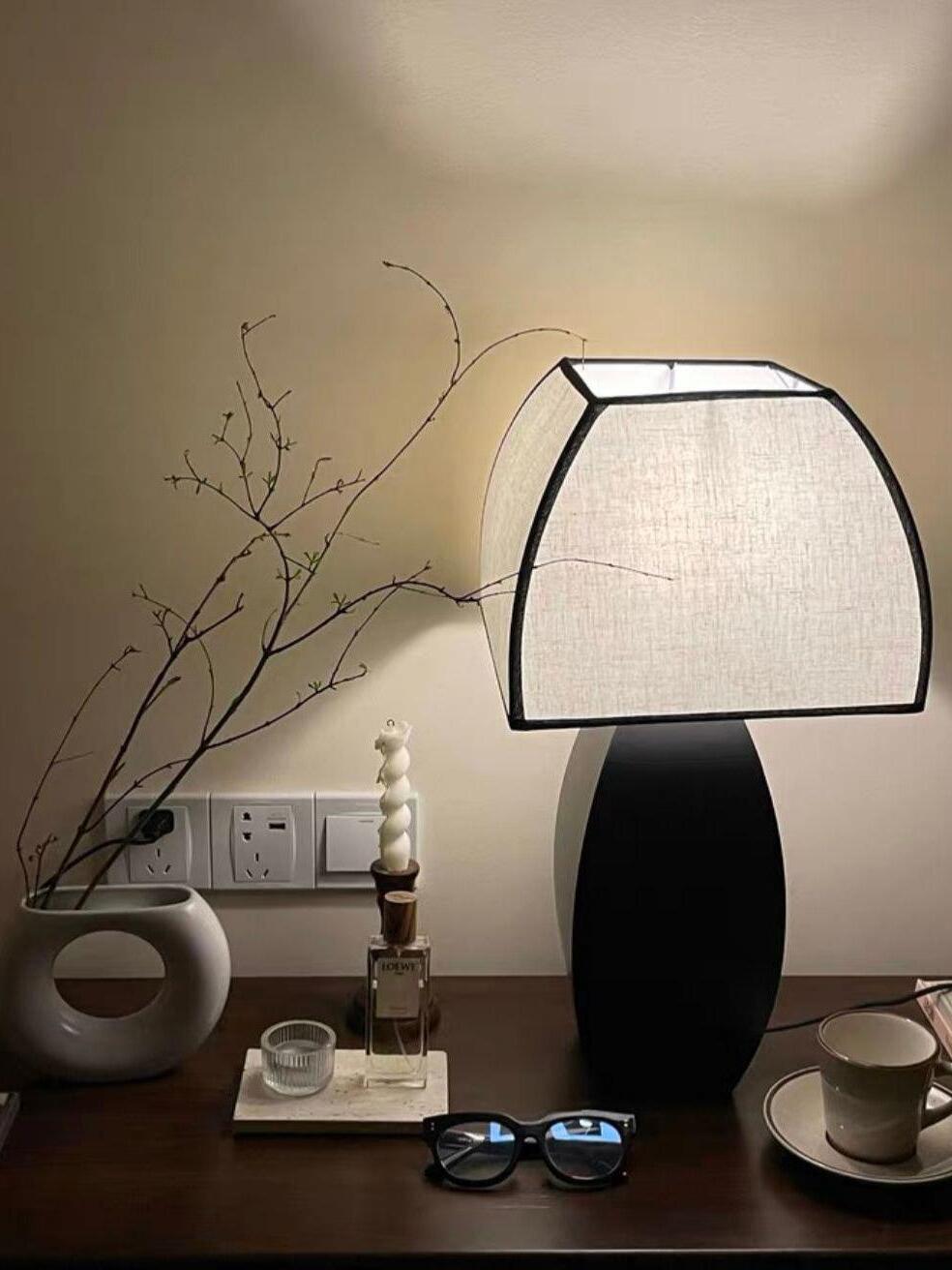Lit fabric-shade lamp on dark table with cup