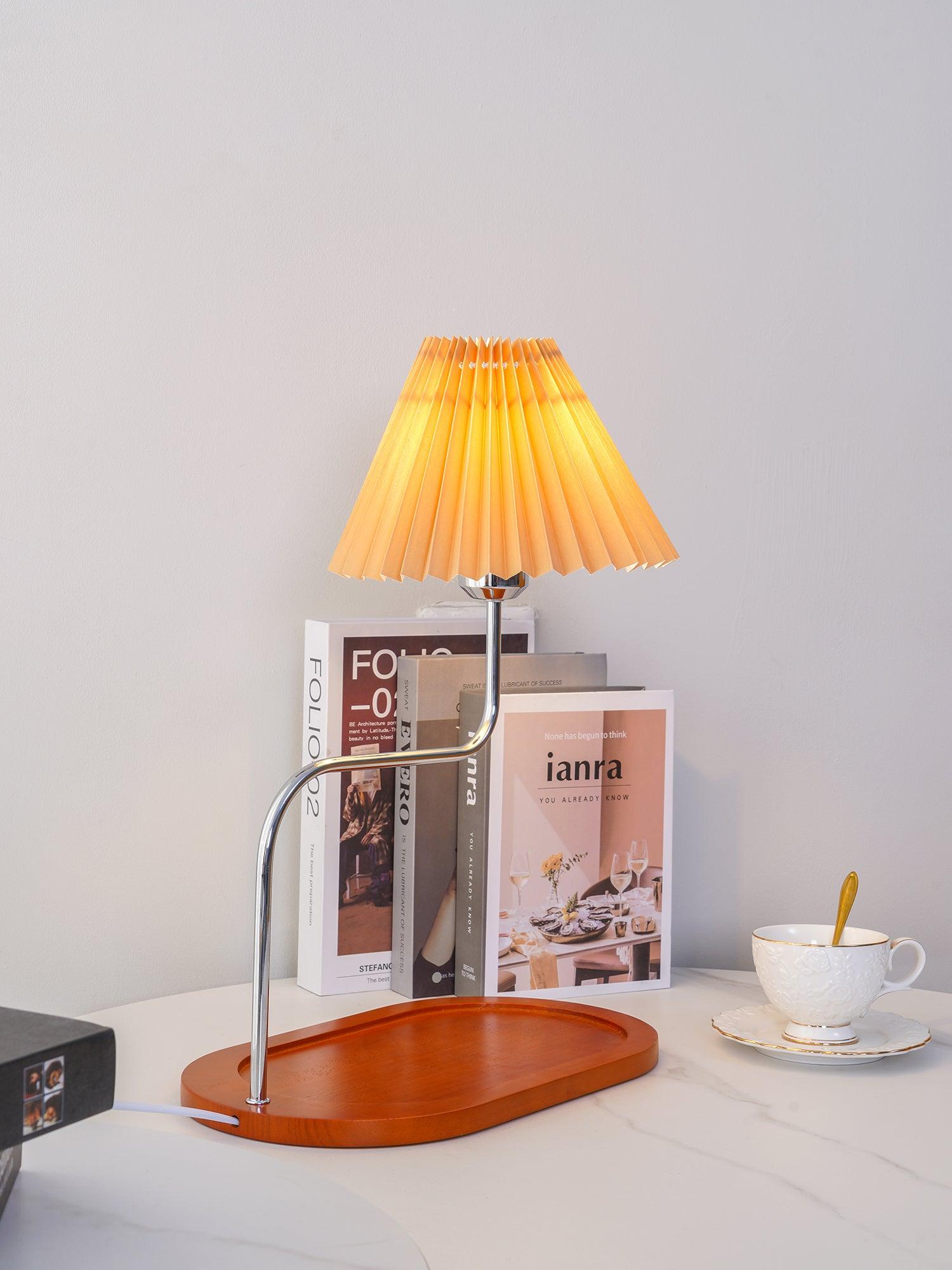 Lit pleated table lamp beside cup and books