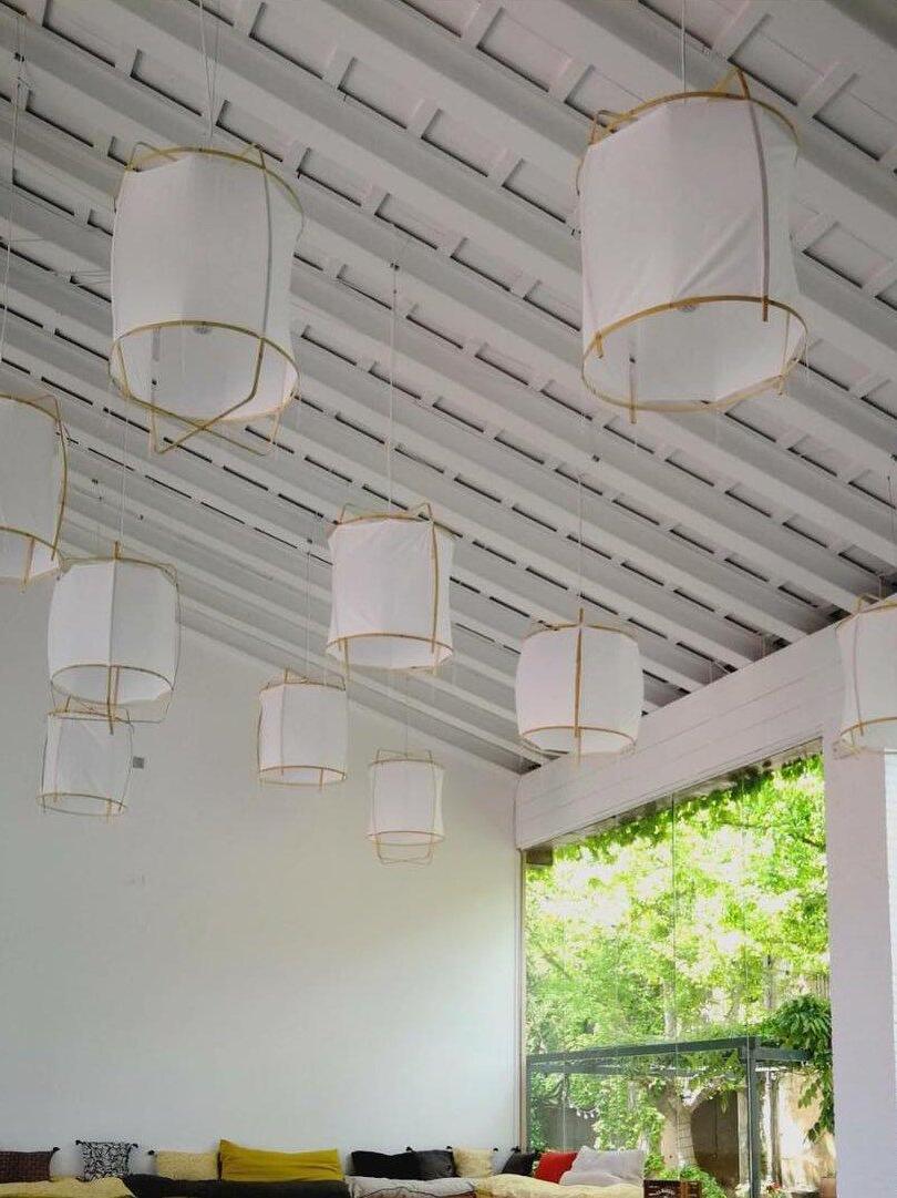 Several white bamboo lantern pendants at varied heights beneath a white beamed ceiling above seating