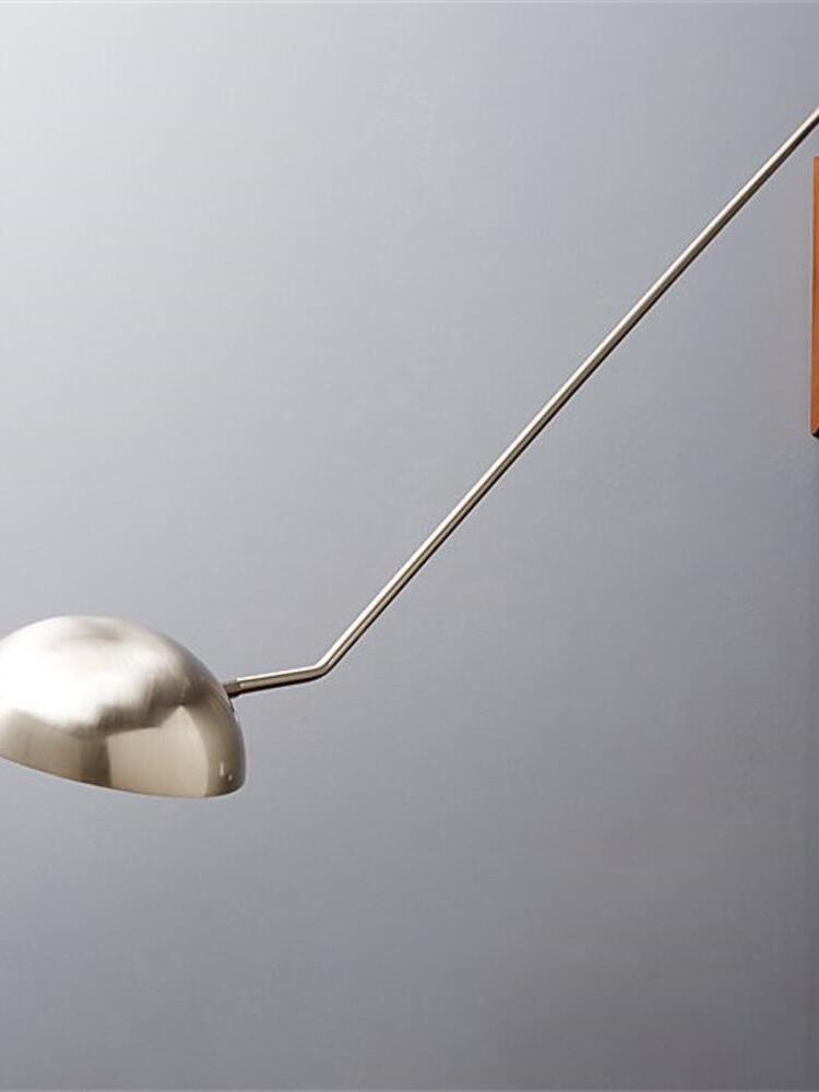 Metallic dome shade and diagonal arm against a grey wall, with a cropped wooden mounting block at right