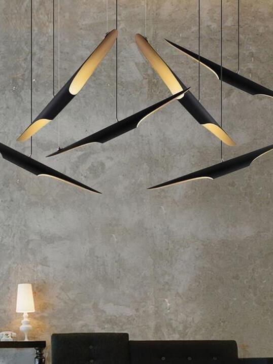 Black and gold pipe pendants at varied angles before a gray textured wall above seating