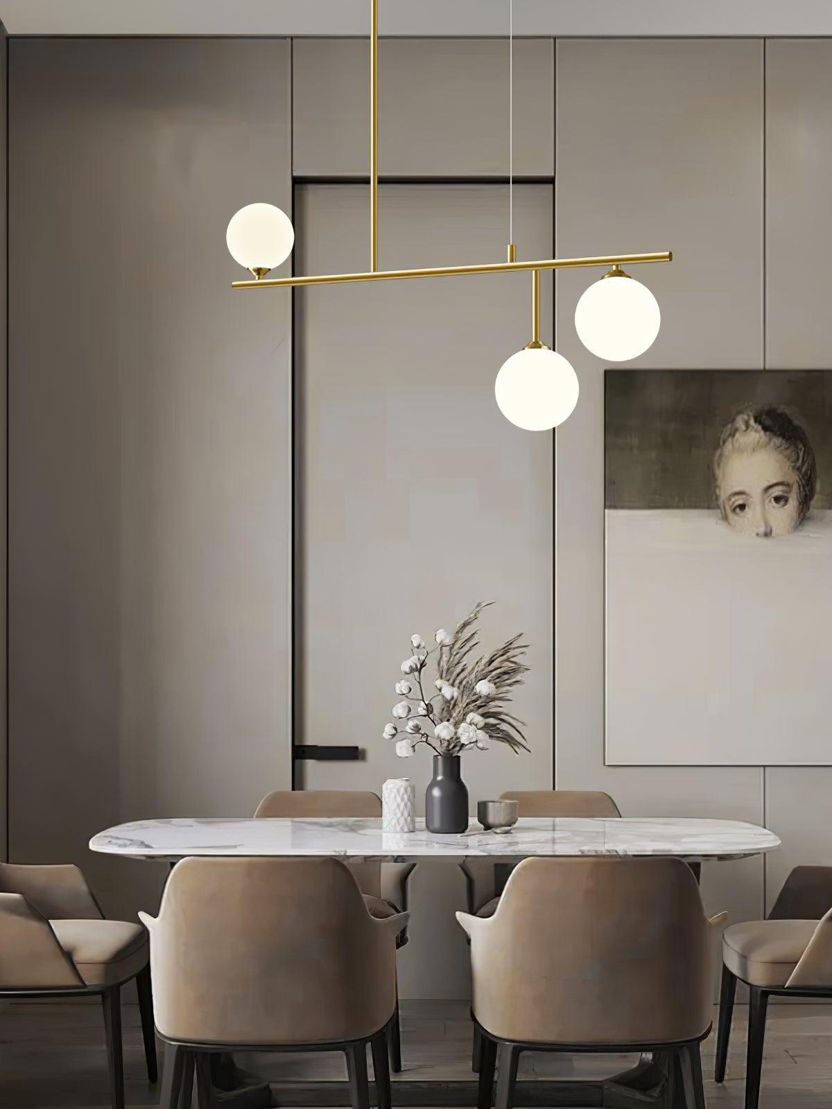 Three-globe Arteriors chandelier over a pale dining table with upholstered chairs, a vase and framed portrait