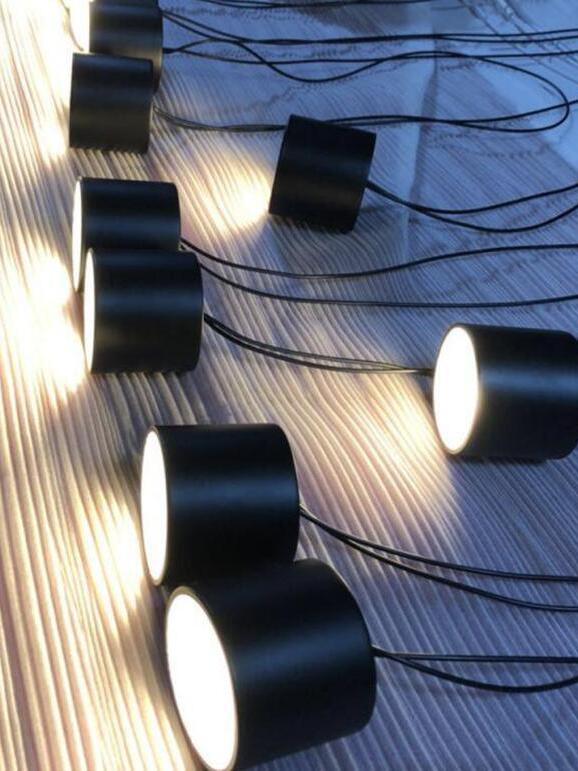 Black cylindrical light heads with glowing circular faces and thin wires resting on striped fabric