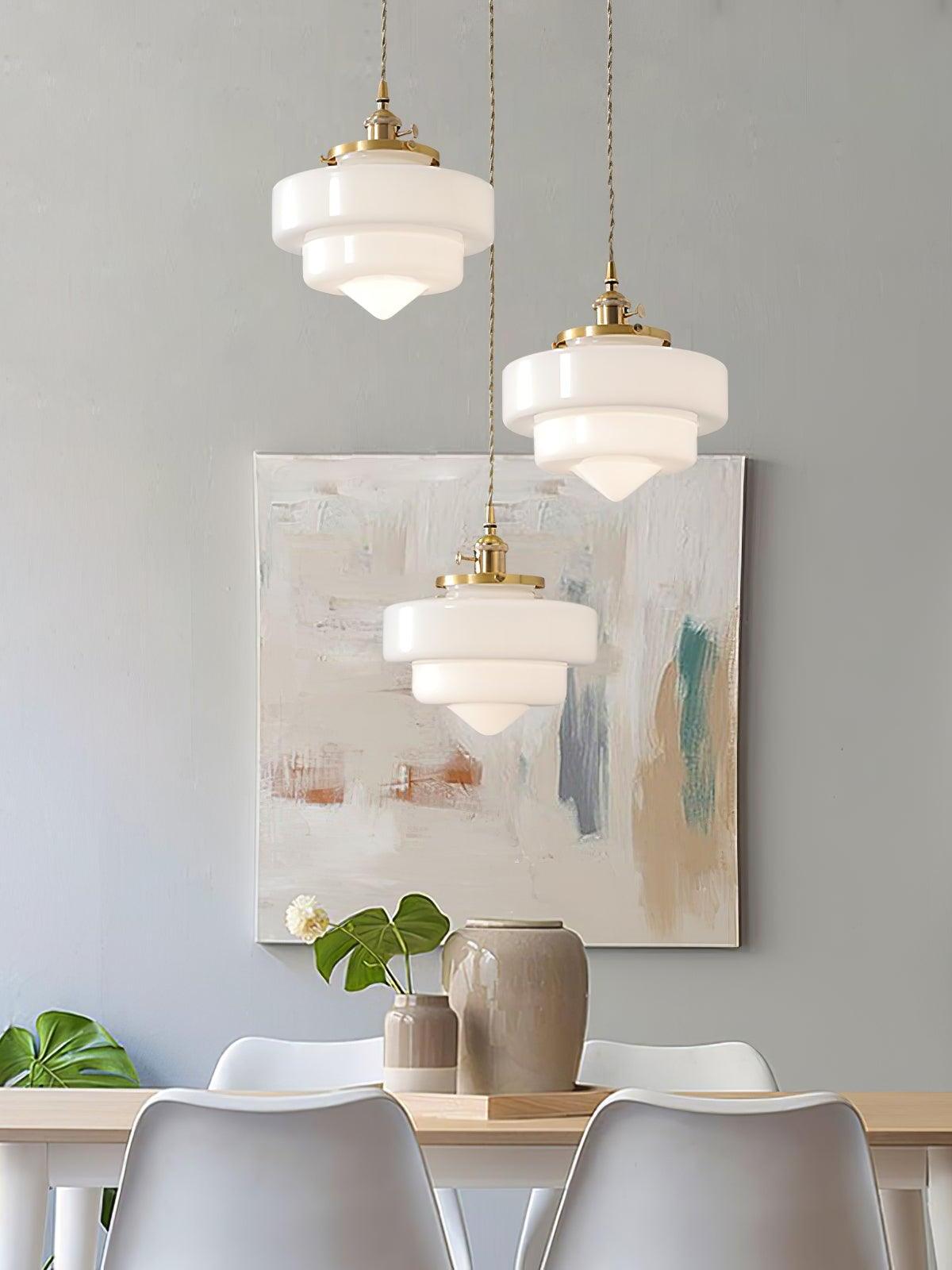 Three lit Atlas Model A white glass shades above a wooden dining table with jars and plants against a gray wall