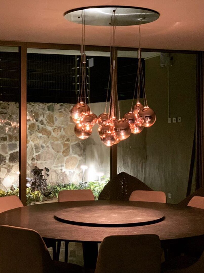 Rose-gold bubble clusters beneath a large oval ceiling plate above a round wooden dining table and pink chairs