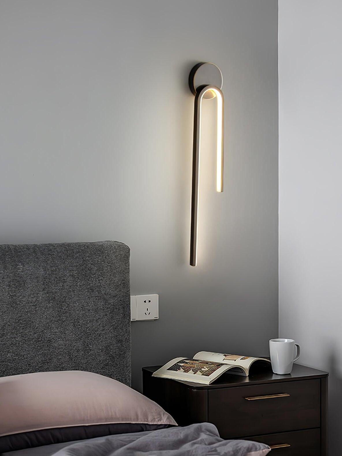 Dark arch beside a gray bedhead above an open book and mug on a black bedside cabinet