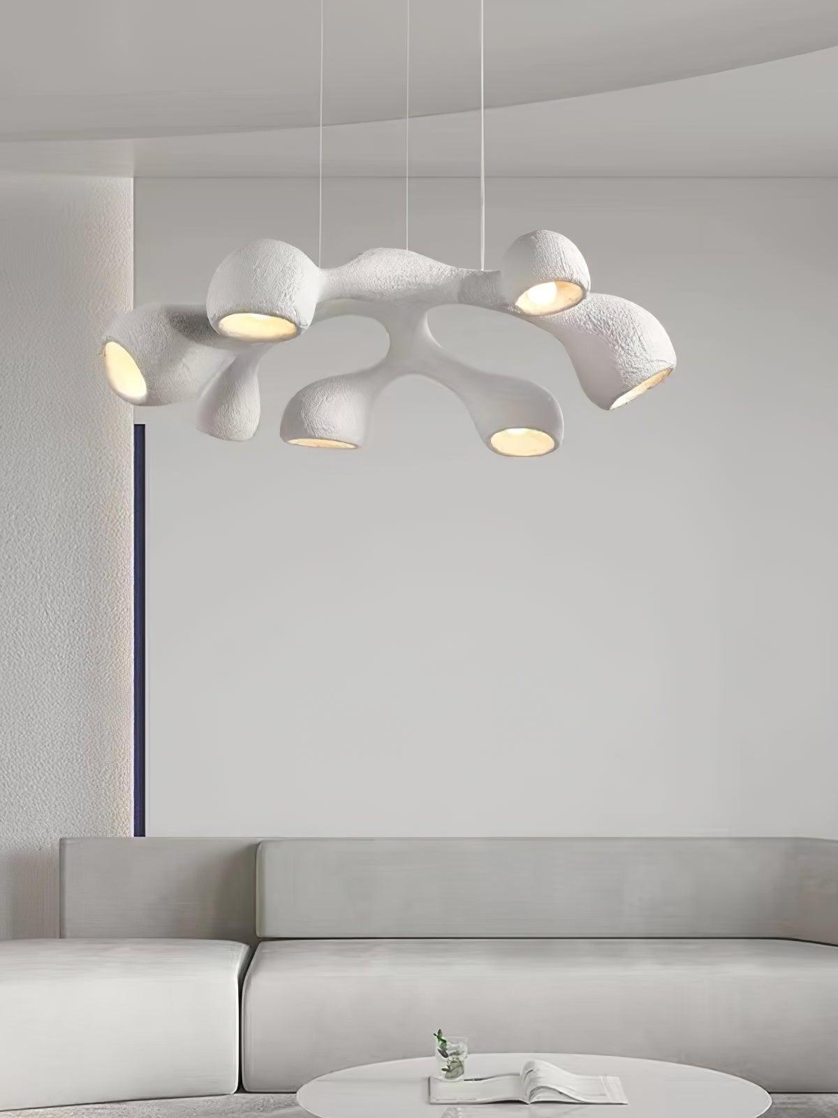 White looped pendant with glowing openings above a pale curved sofa and round table with an open book