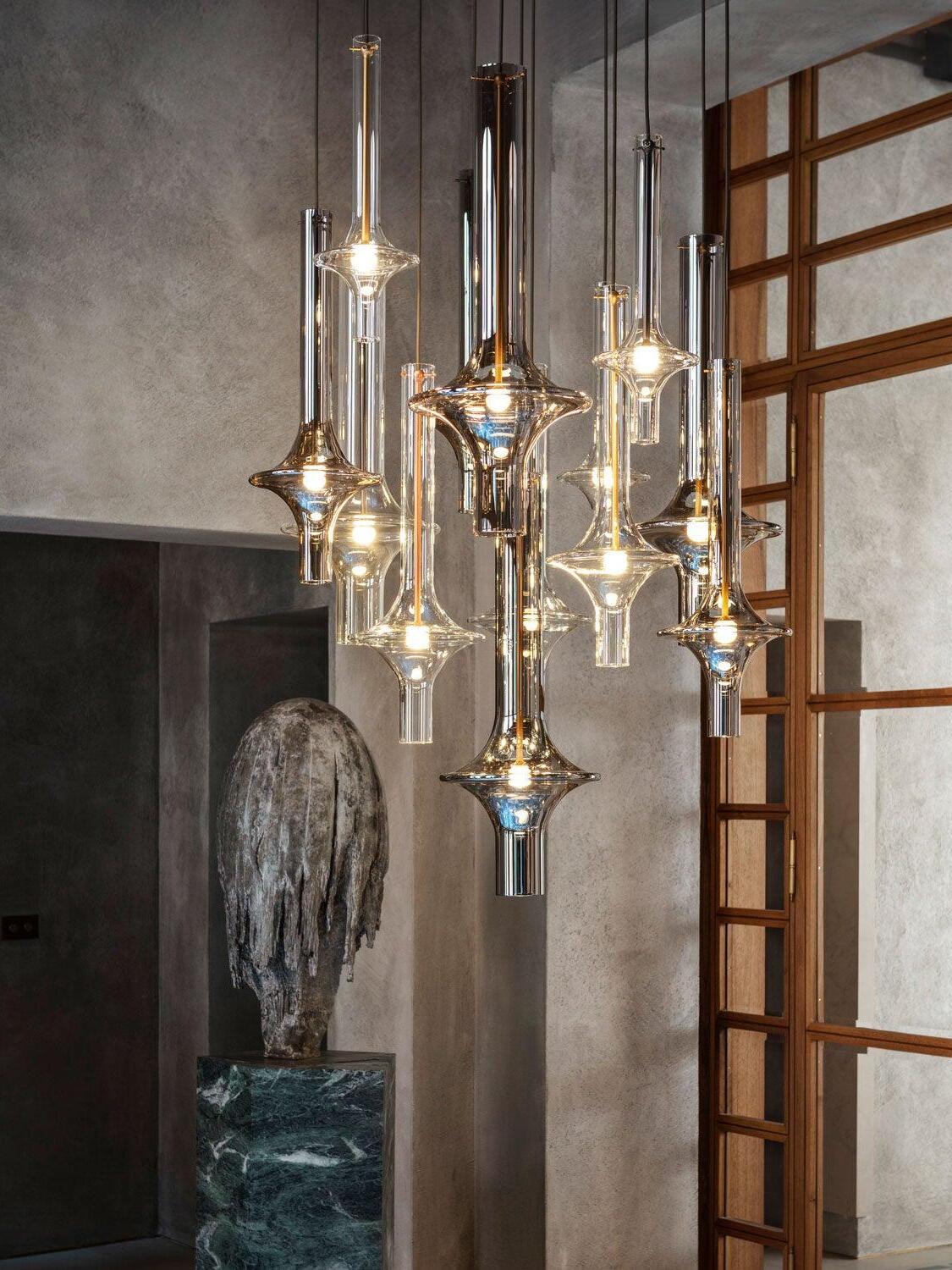 Mixed clear and smoky glass pendants at varied heights beside a wooden window grid and stone sculpture