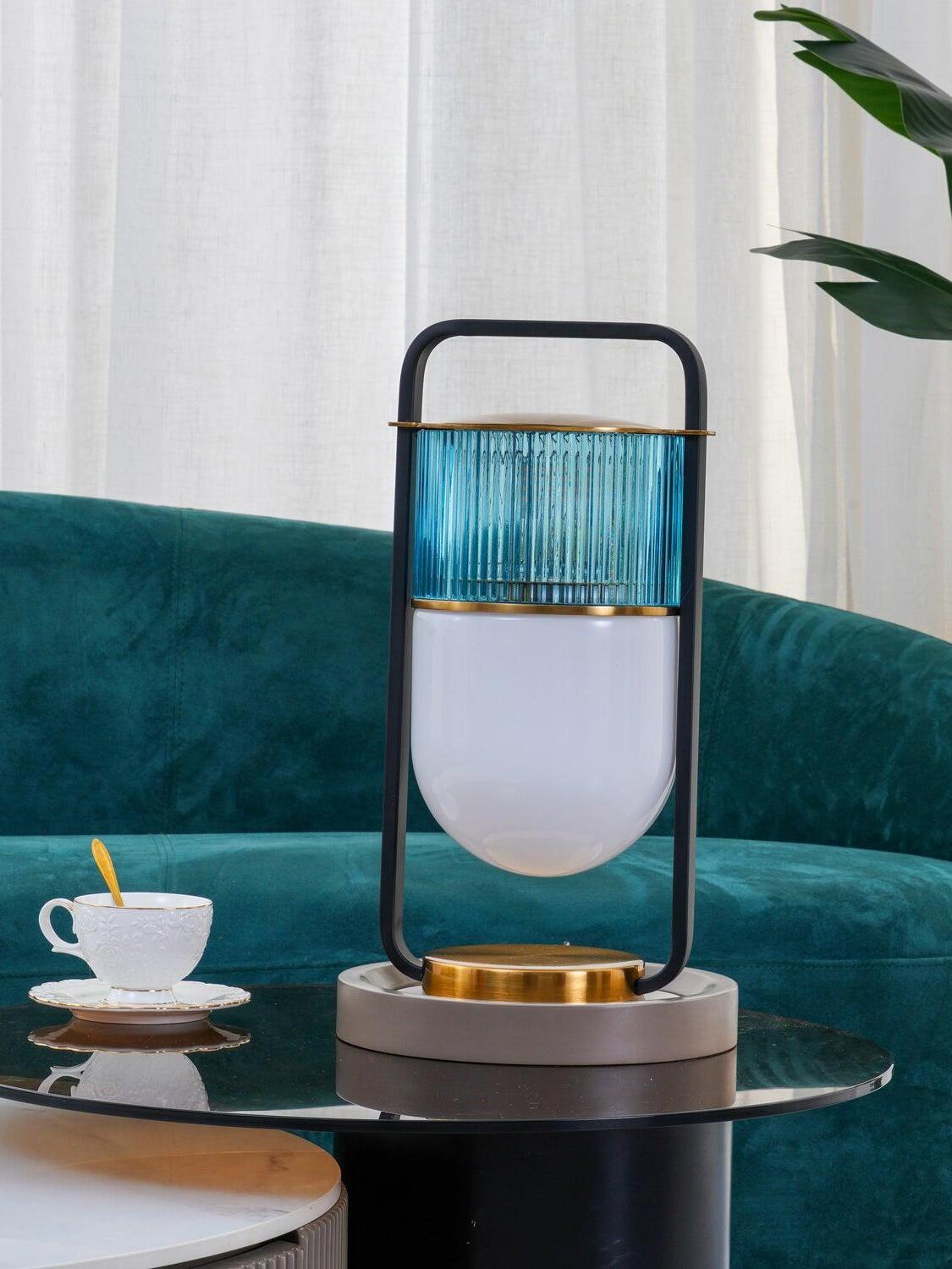 Unlit Xi lamp with blue-green ribbed upper glass on a pale round pad beside a cup and teal sofa