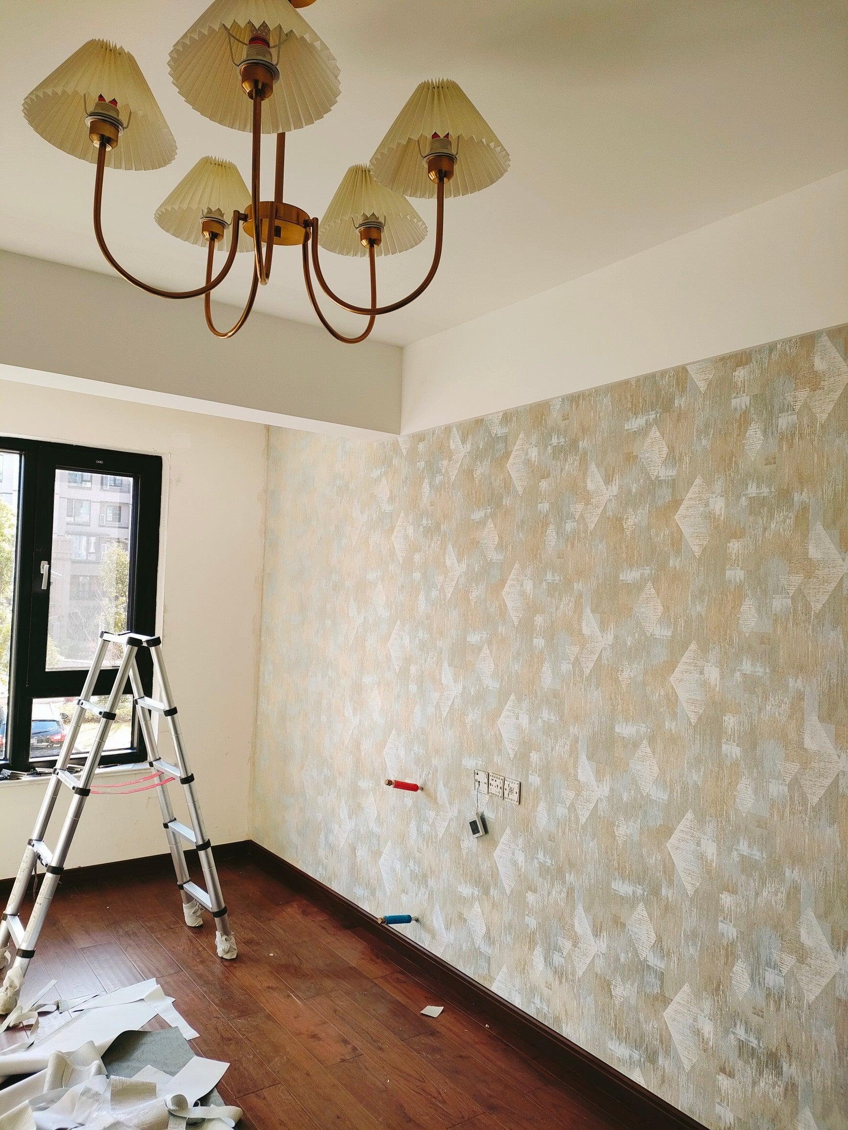 Low-angle chandelier view in an unfinished room with a ladder and patterned wallpaper