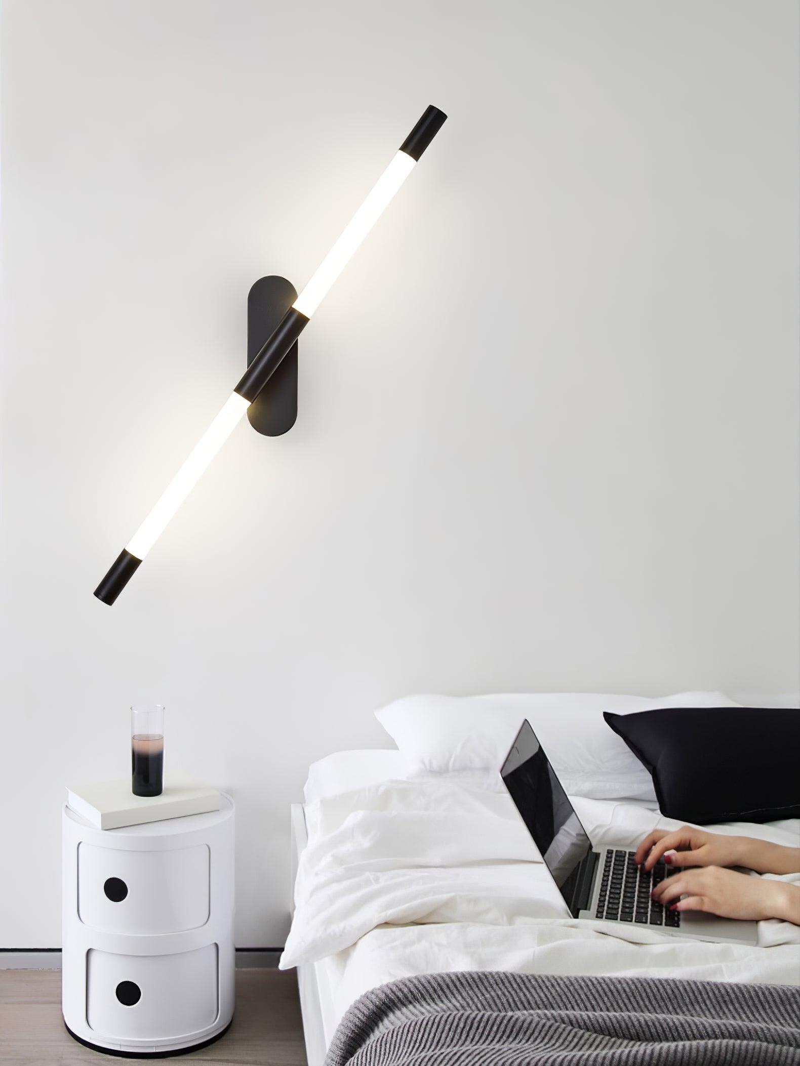 Angled black Agnes wall light beside a bed and a white cylindrical object