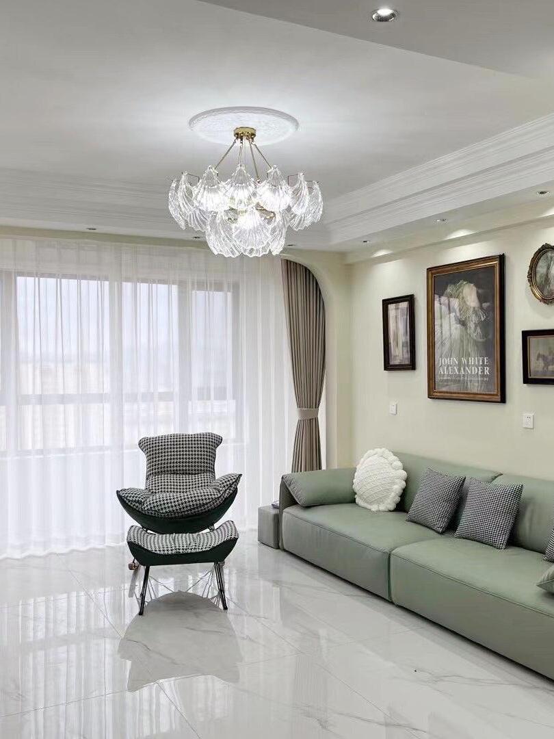 Round glass ceiling light above a green sofa and lounge chair beside a bright window