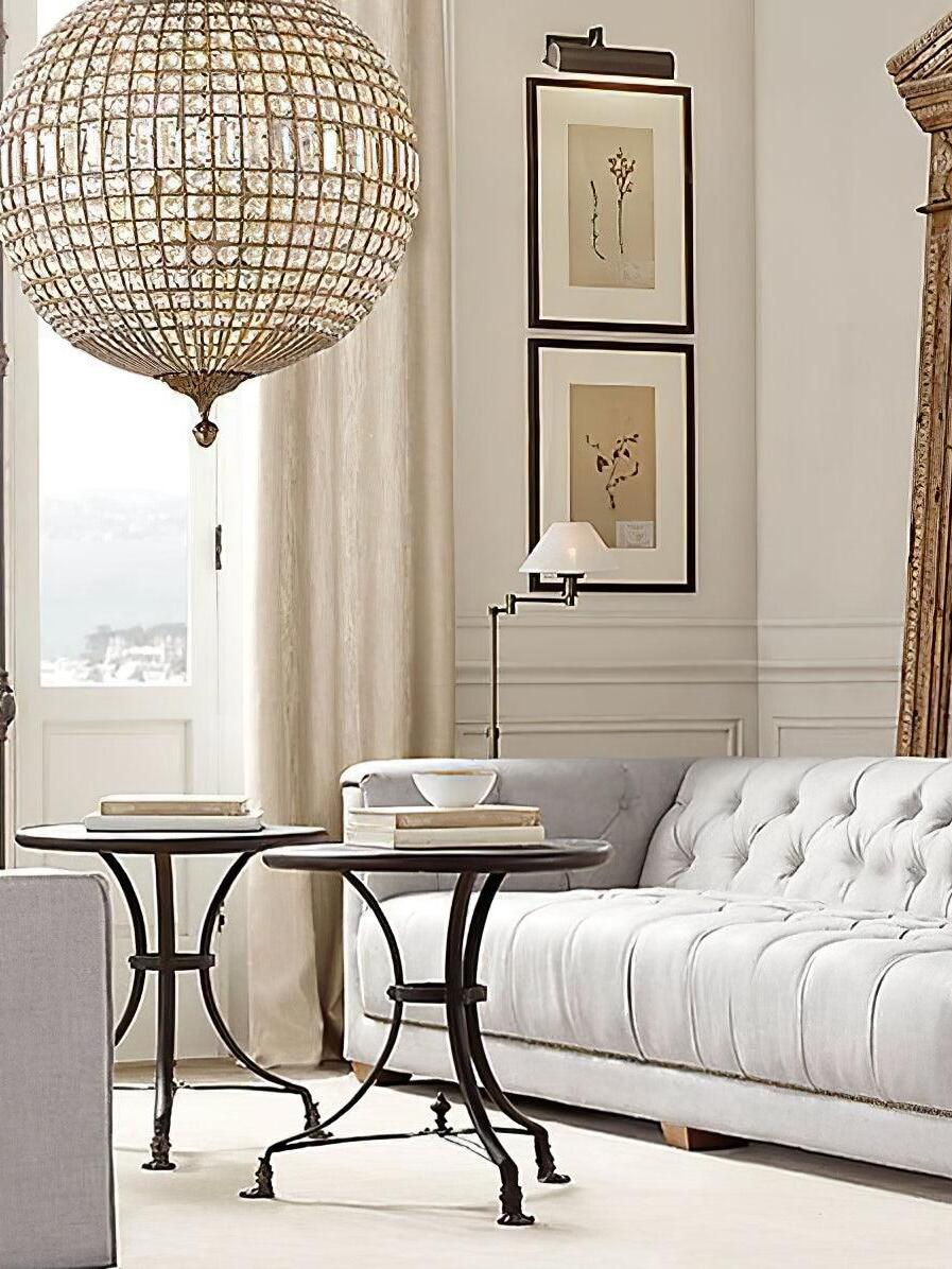 Cropped glowing crystal globe above a pale tufted sofa and round side tables beside a window