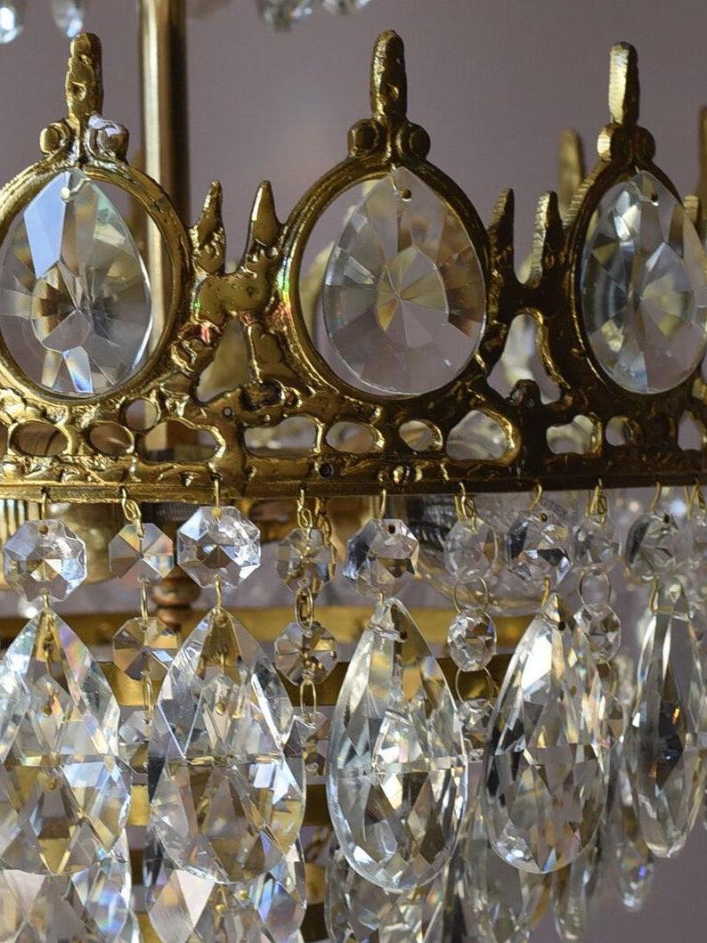 Close view of dark gold-tone crown details, round faceted inserts and linked clear crystal drops