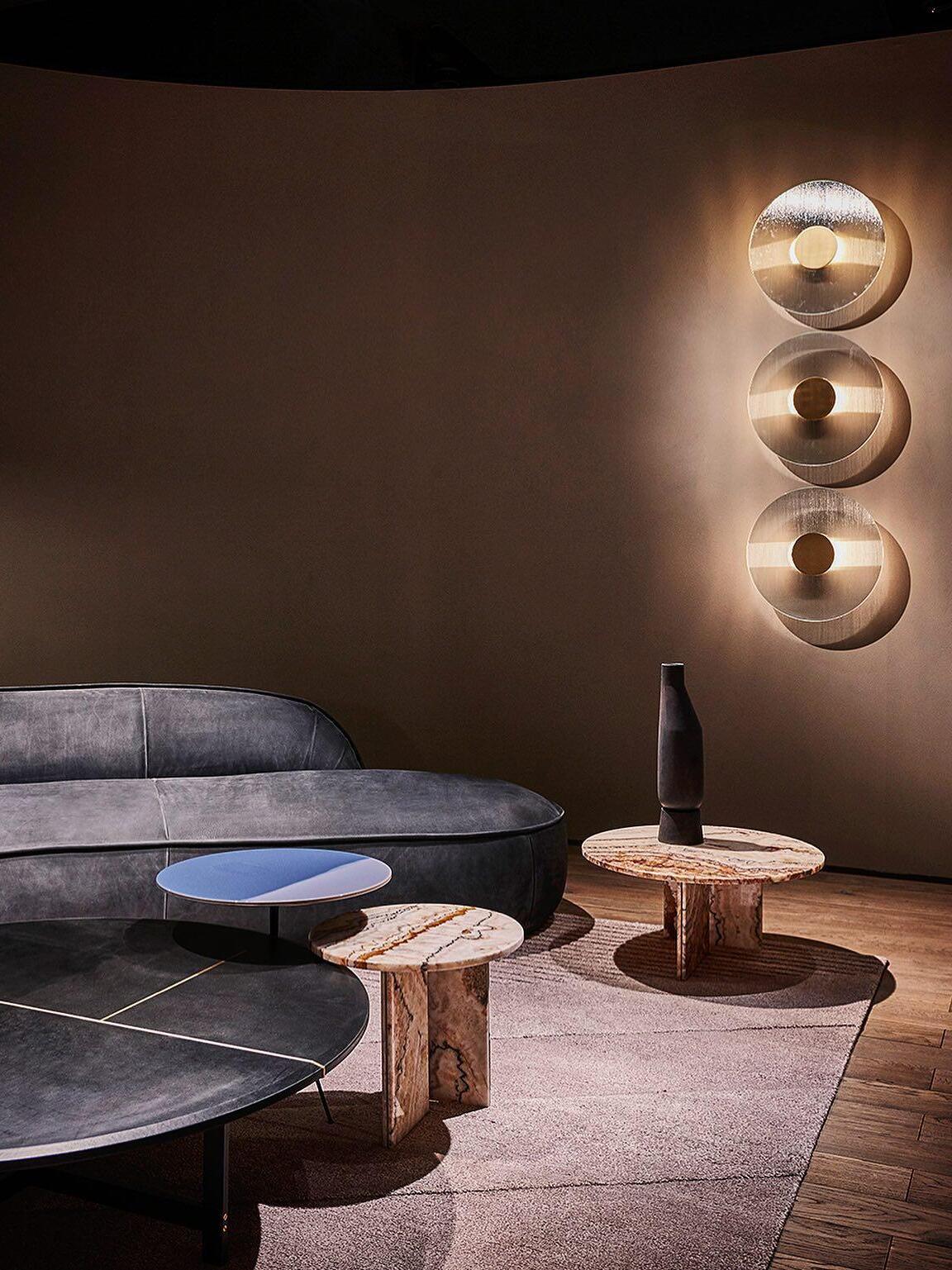 Three round Button wall lights above a curved grey sofa with a blue dish, stone-patterned tables and black vase