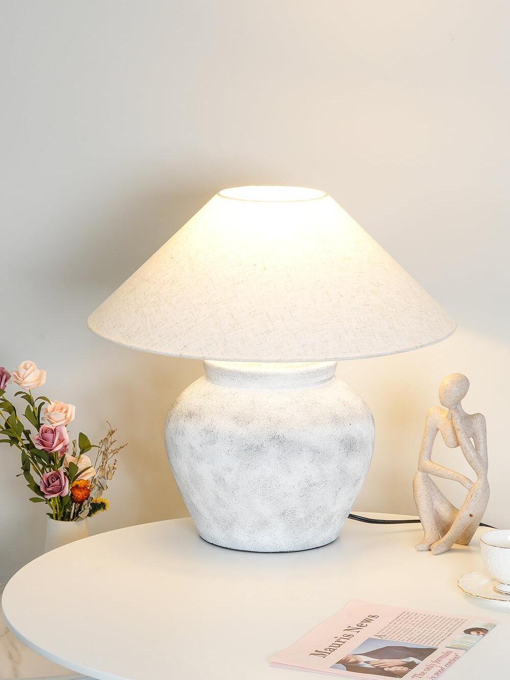 Glowing urn table lamp near flowers and figurine