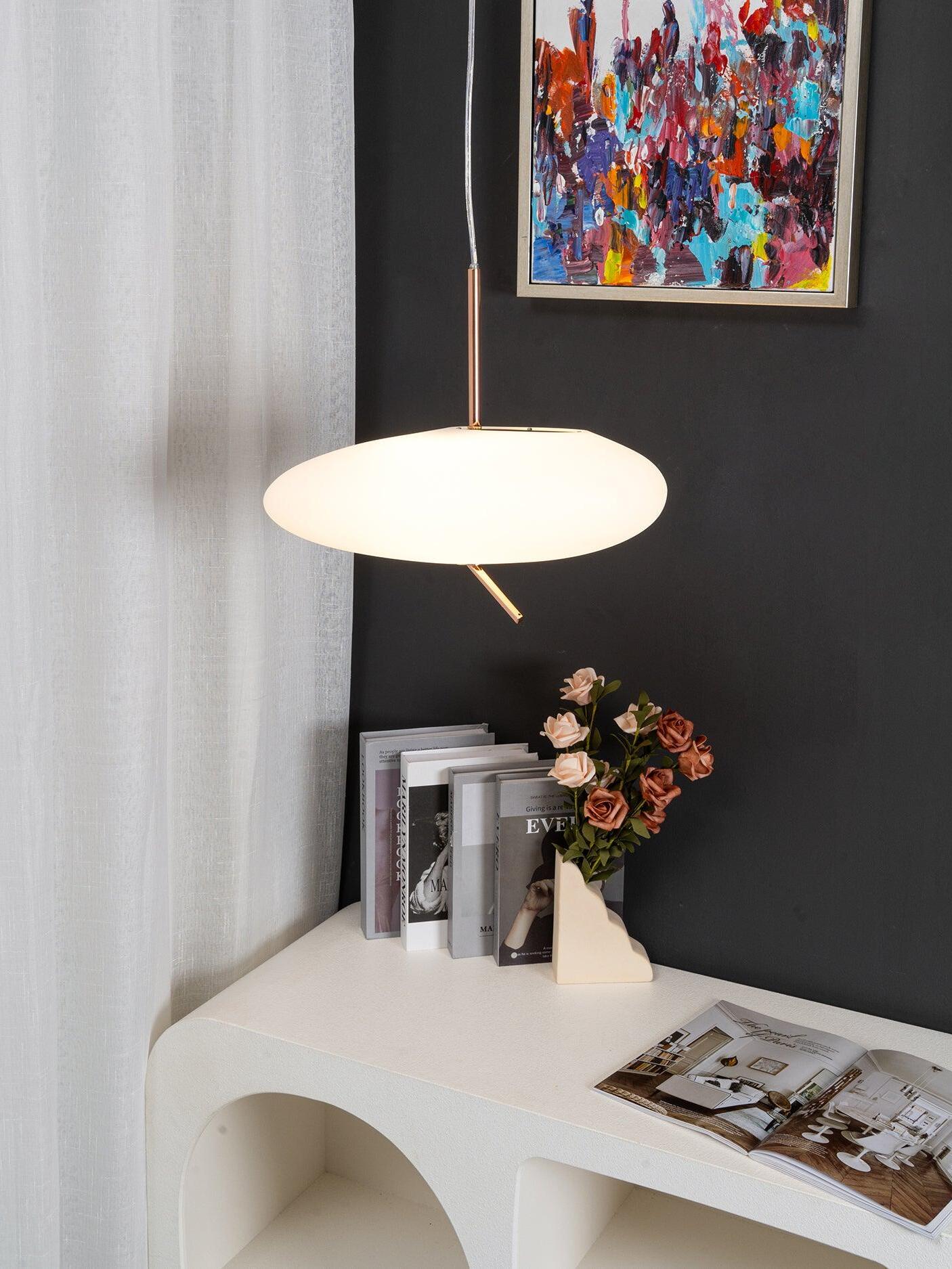 Lit white pendant with a rose-gold stem above a curved console with flowers and an open book