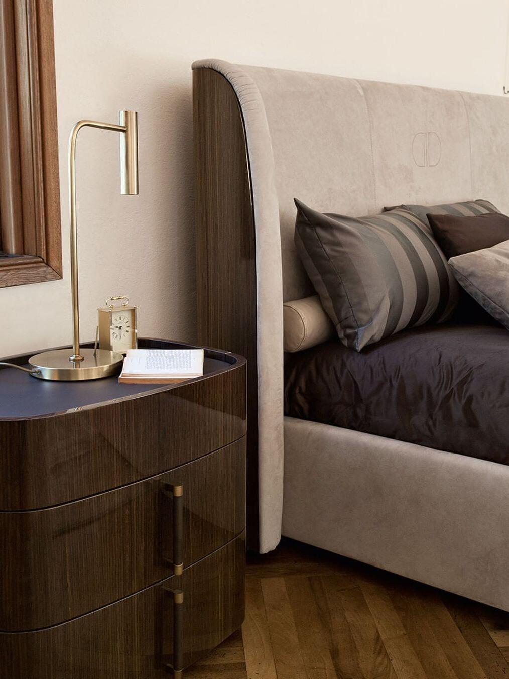 Gold-tone slim lamp on bedside cabinet with mug, book and upholstered headboard