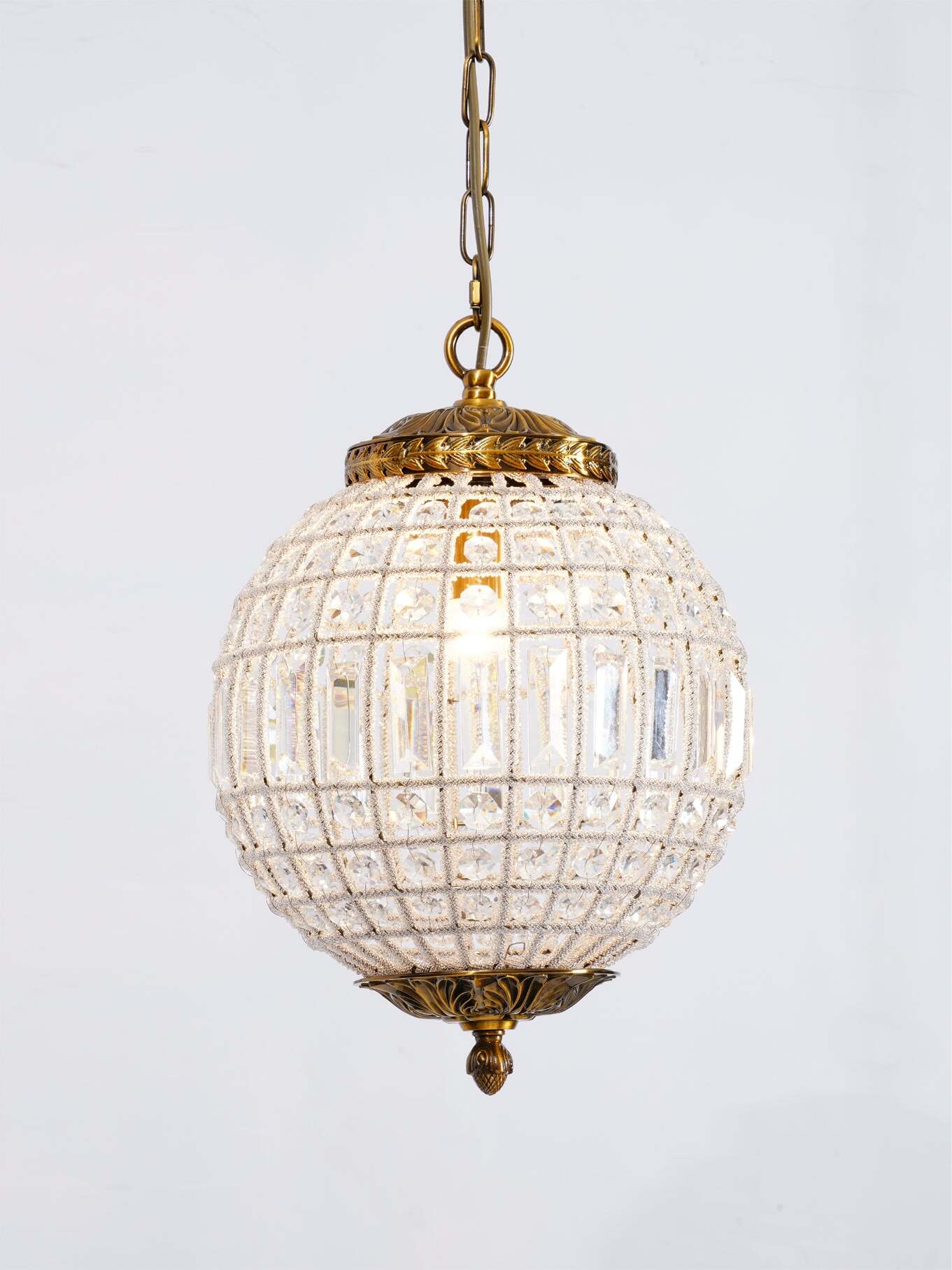 Close lit globe with rows of round crystals, rectangular middle pieces and a gold-tone leaf-pattern cap
