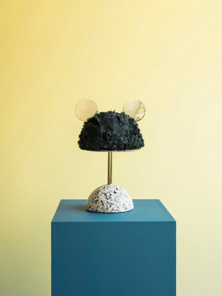 Dark plush lamp on blue display cube against yellow wall in wider crop