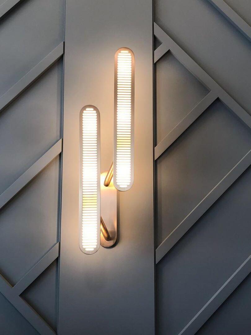 Lit staggered vertical grille bars on one gold-tone backplate against a Gray wall with diagonal paneling