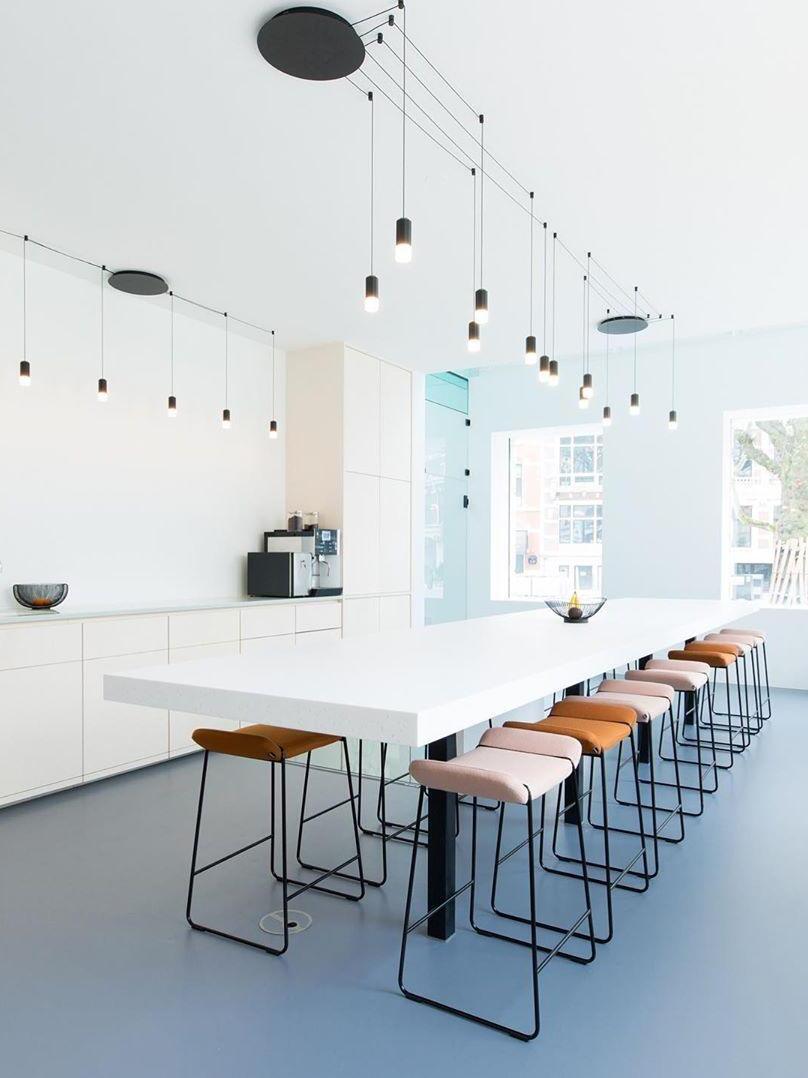 Black routed ceiling cables and pendant heads above a white counter with stools