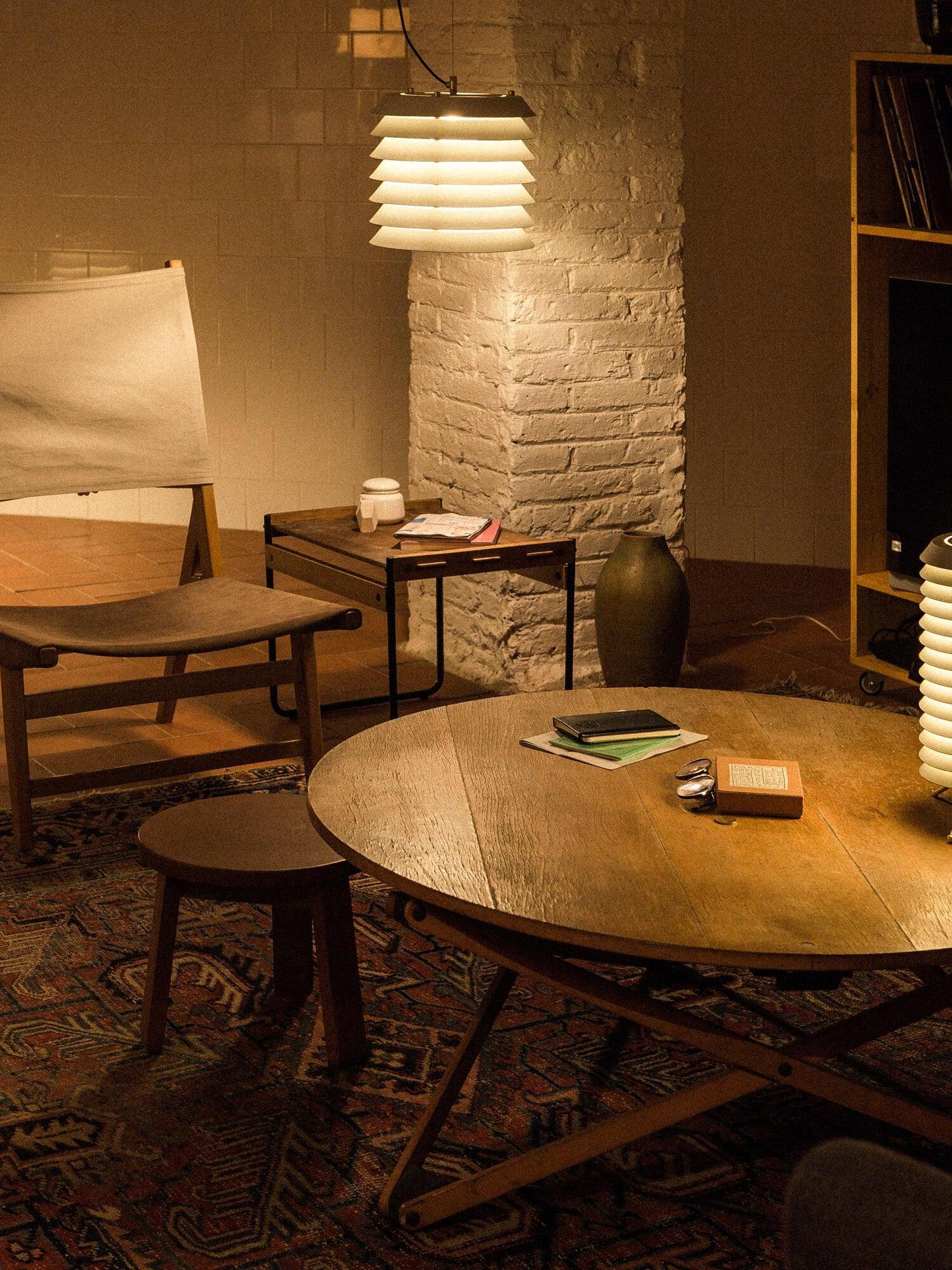 Lit white layered pendant over wood table and upholstered chair near brick pier
