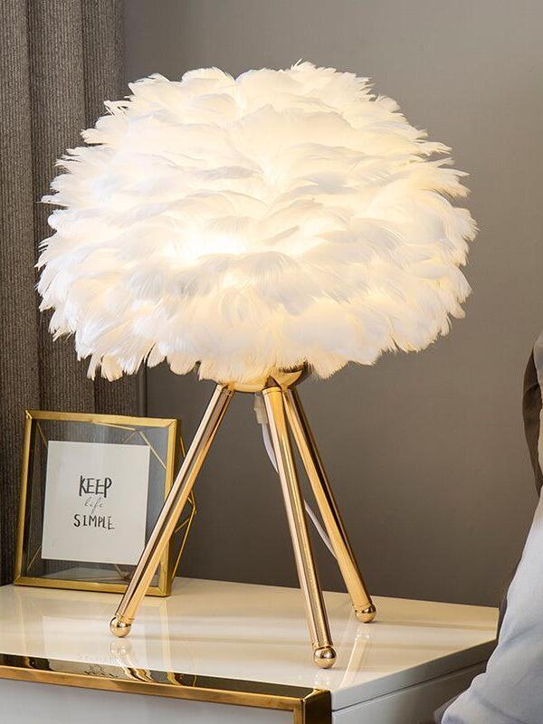 White feather lamp on gold tripod beside framed art