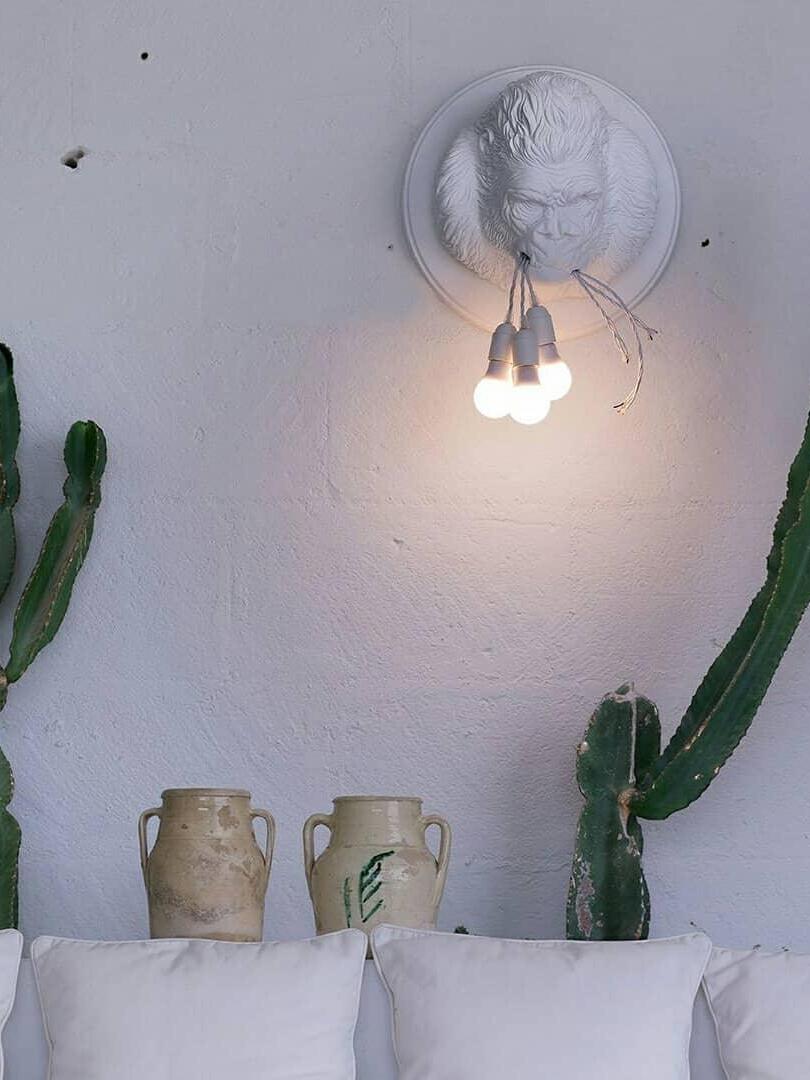 White gorilla wall light above indoor decor and cactus on pale wall