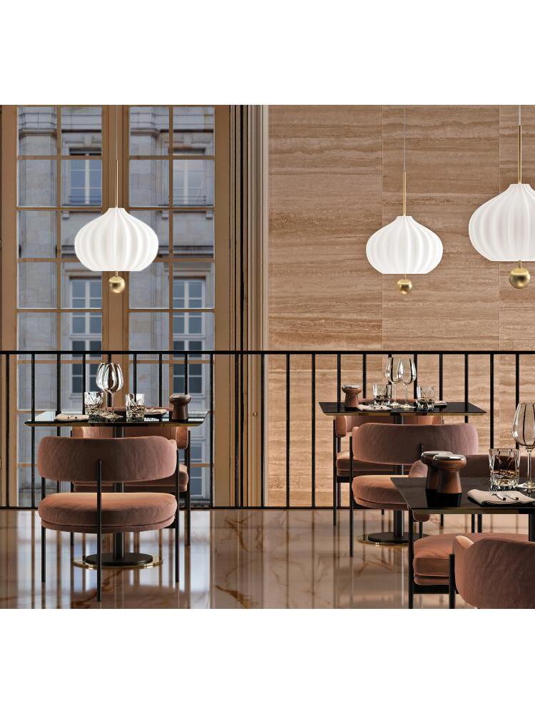 Wide restaurant view of white fluted pendants above dark tables and pink chairs beside large wooden windows