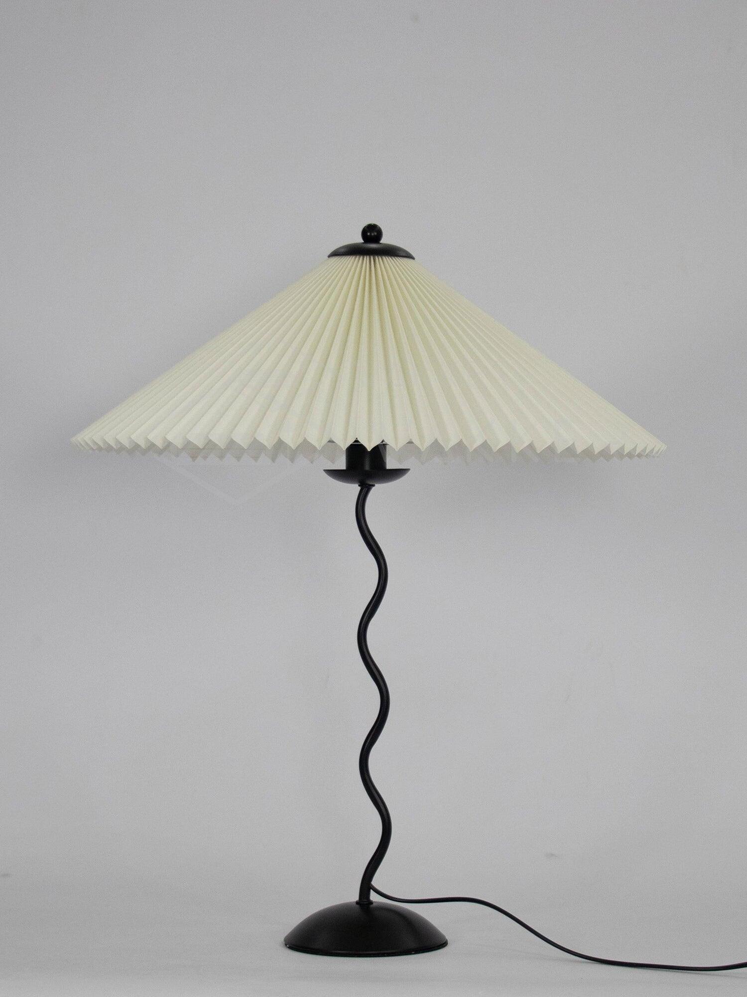 Cream-shade Squiggle lamp with black wavy stem, round base and power cord on a pale background