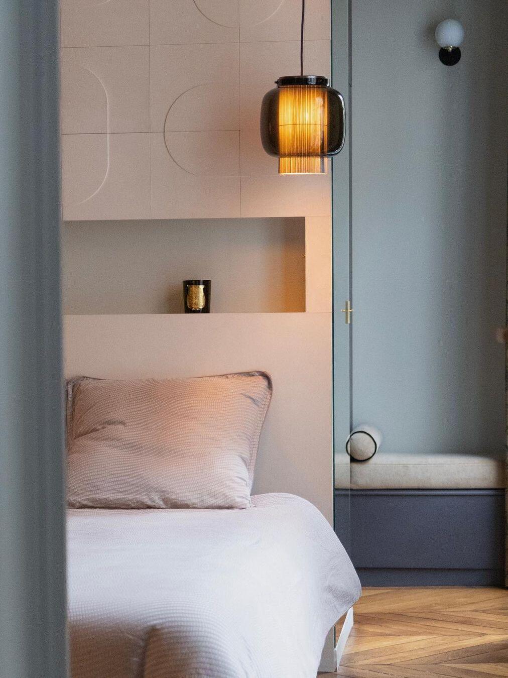 Small black and smoke-grey Manila T pendant beside pale bedding and a wall niche, with a separate wall light