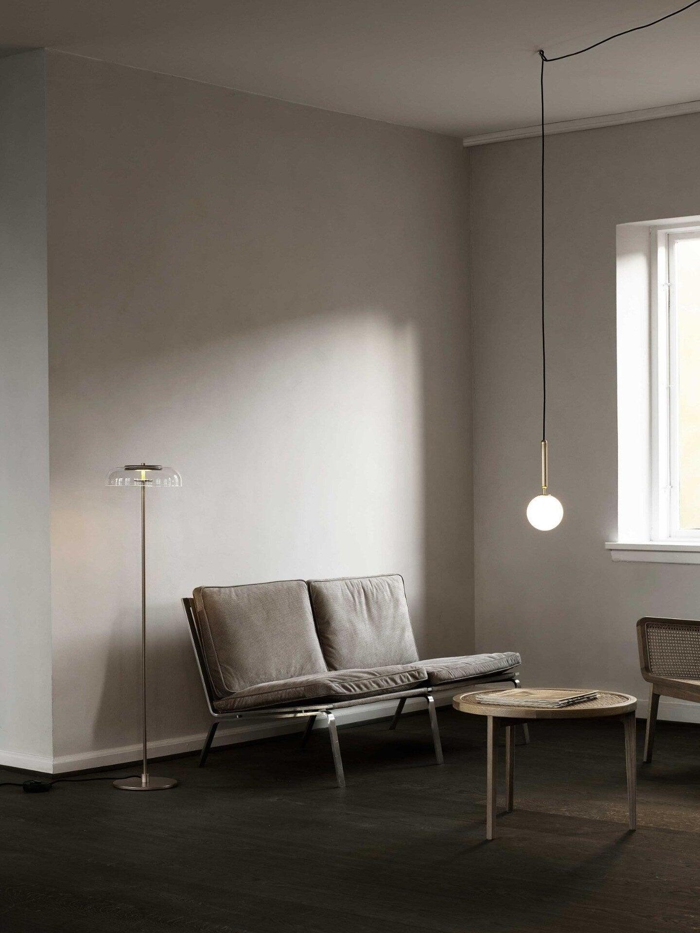 Single white globe pendant on a routed black cord above a gray sofa beside a separate floor lamp