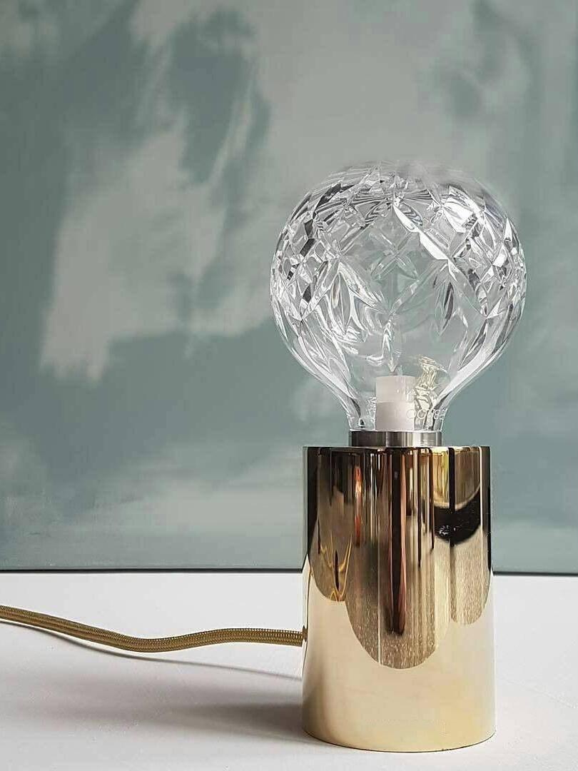Clear faceted globe lamp with gold-colour cord against green-grey wall