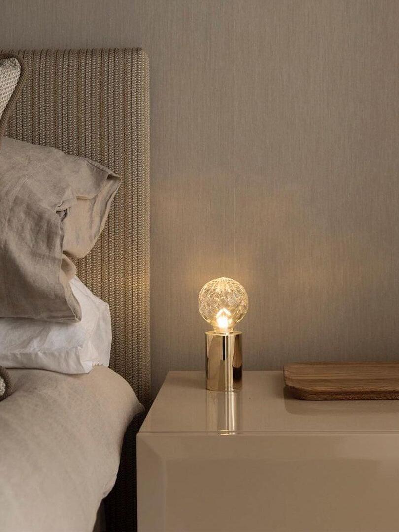 Small glowing globe table lamp on bedside cabinet near beige bed