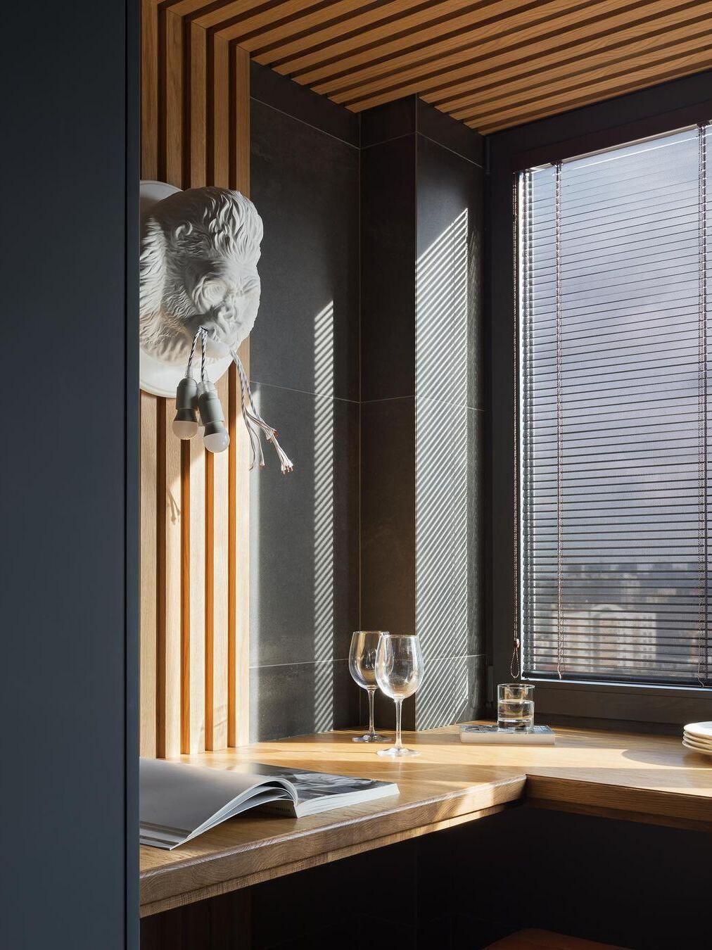 White gorilla wall light in wood-slat window nook above book and glass