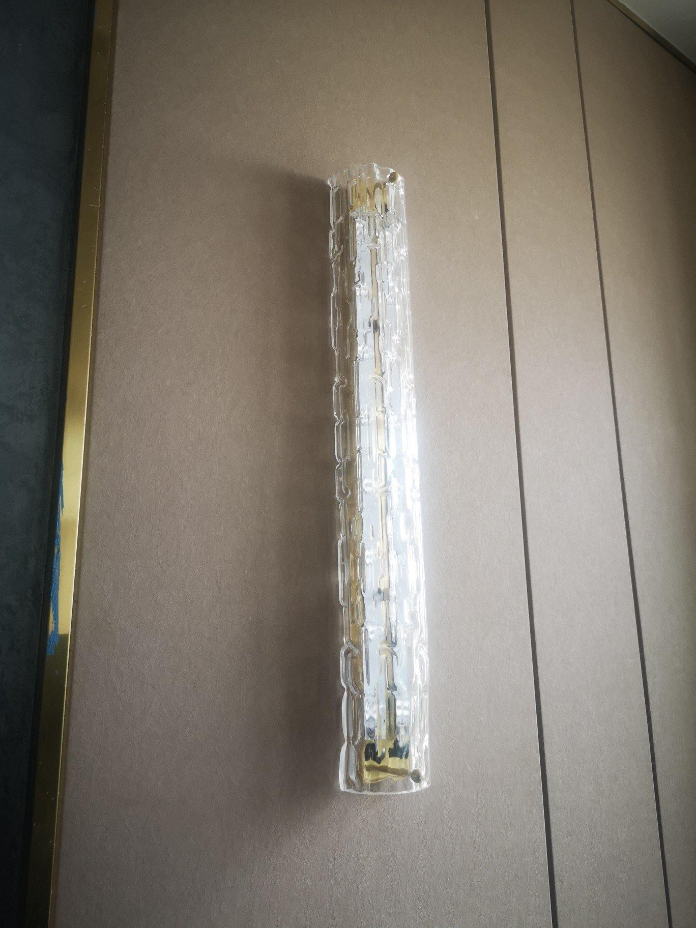 Unlit clear glass wall light on angled pale wall panel